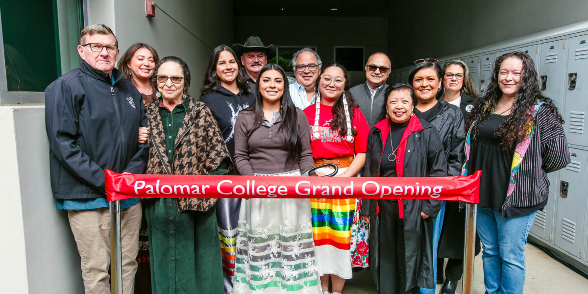 A large group stands behind a red ribbon labeled "Palomar College Grand Opening" holding large scissors next to a concrete building.