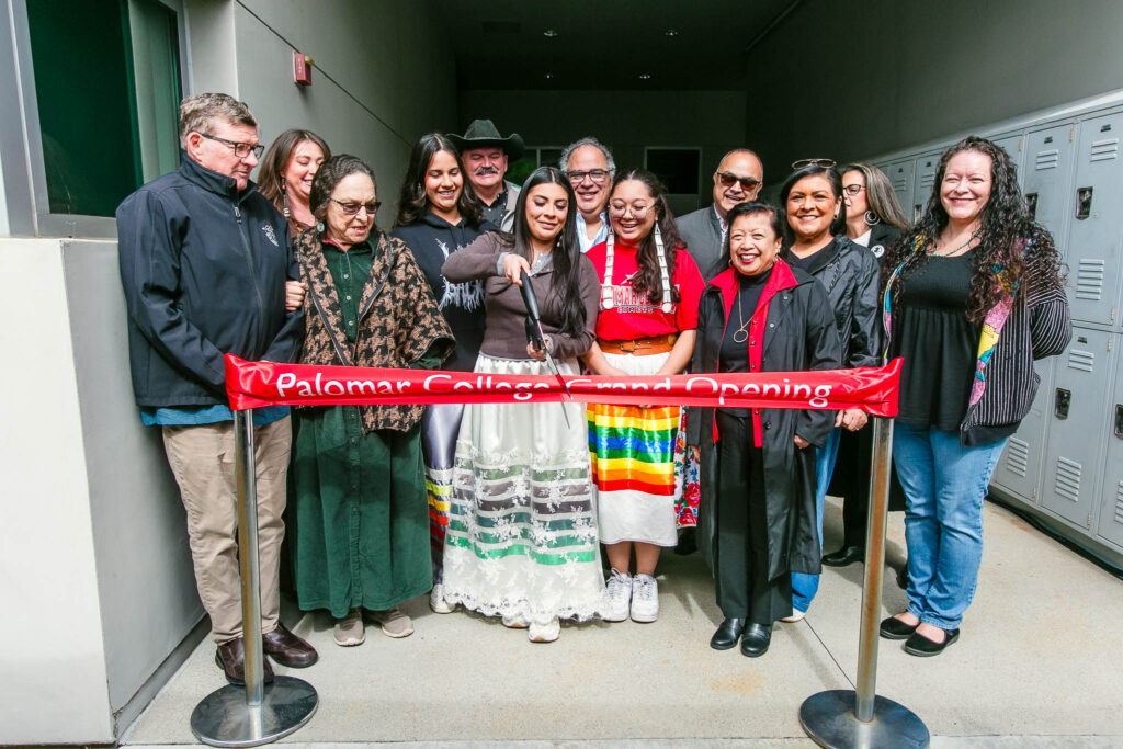 A large group of people prepare to cut the ribbon for the opening of a center at an event.