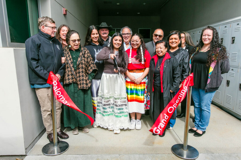 A group of people smile as the ribbon is cut to signify the Grand Re-Opening of the Native American Resource Center.