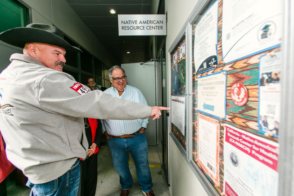 People gather near a bulletin board filled with flyers and announcements mounted next to the Center entrance door.