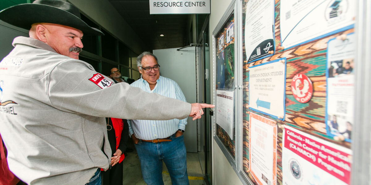 People gather near a bulletin board filled with flyers and announcements mounted next to the Center entrance door.