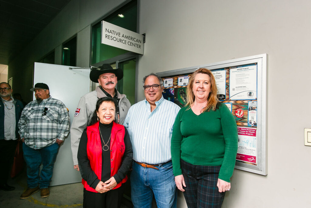 Several people stand in front of a bulletin board under a sign that reads "Native American Resource Center."