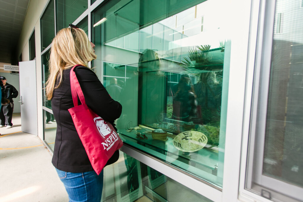 A person standing outside looking through a large window at baskets and other items displayed inside.