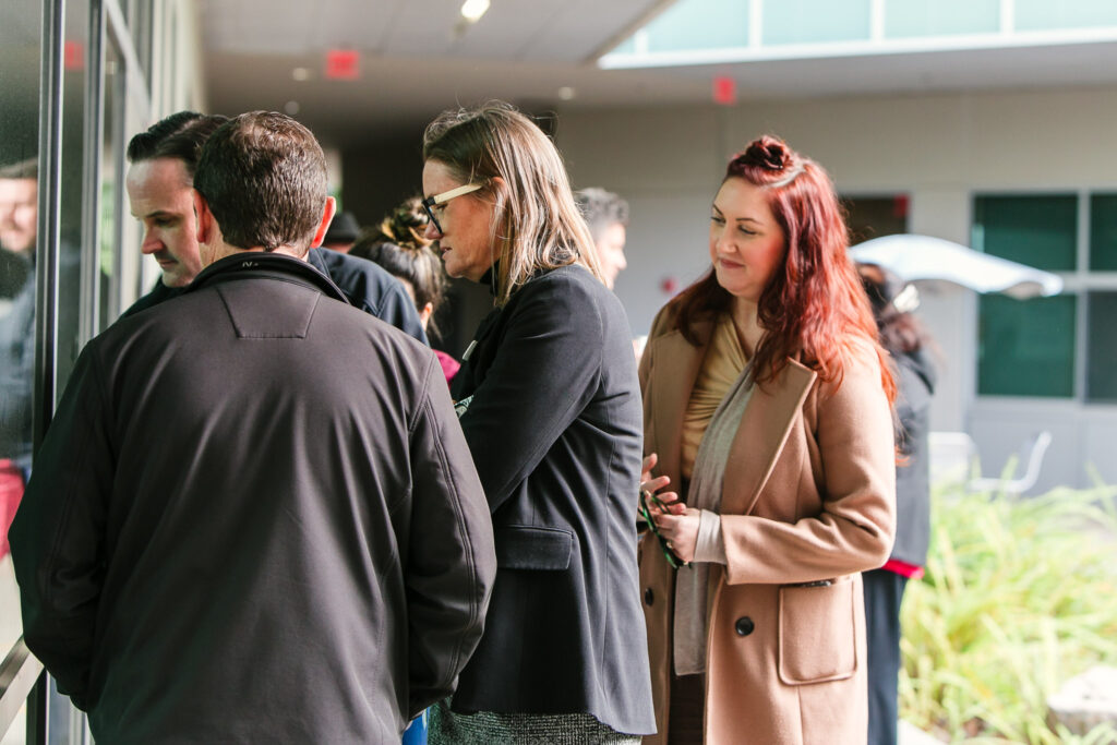 A group standing on an outdoor walkway with windows to the Resource Center on one side and plants on the other.