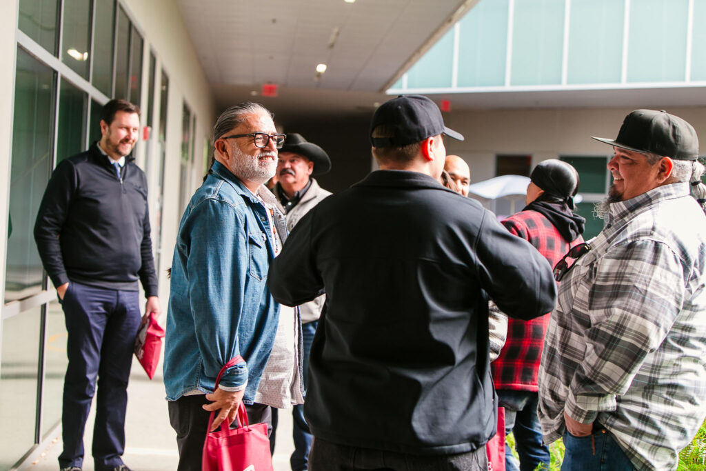 People standing together outside a classroom, holding red tote bags, with buildings and other attendees in the background.