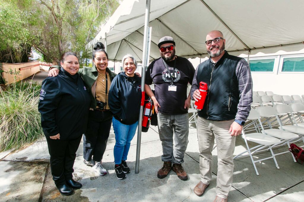 Several people standing under a tent holding red reusable bottles.