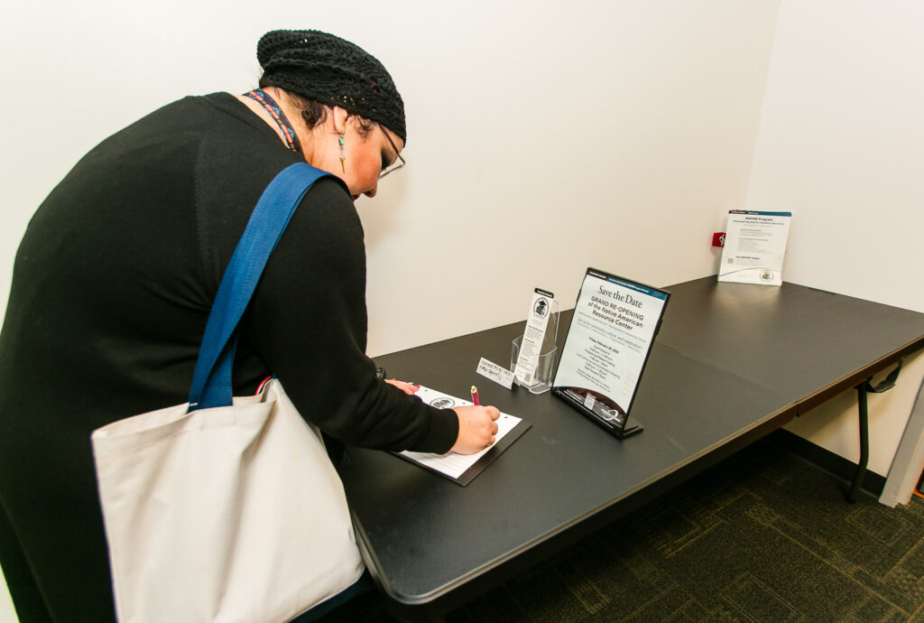 A person writing on a notepad placed on a black table next to event flyers and informational materials.