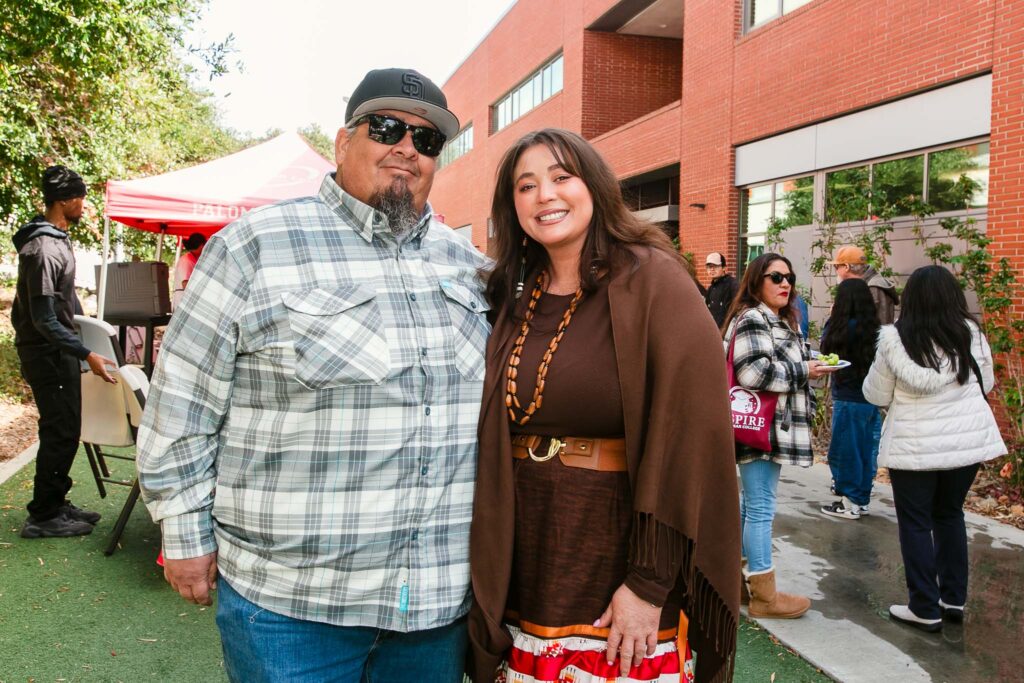 Two people standing side-by-side outdoors on artificial turf near a brick building.