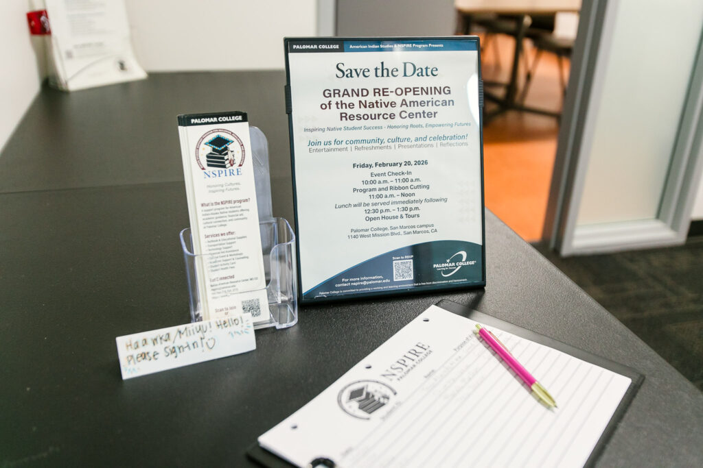 A black table with a framed "Save the Date" flyer, bookmark flyers, a handwritten welcome note, and a notepad with a pink pen.