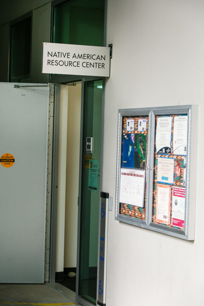 The Resource Center entryway with a metal door and a bulletin board filled with a calendar, flyers, and informational materials.