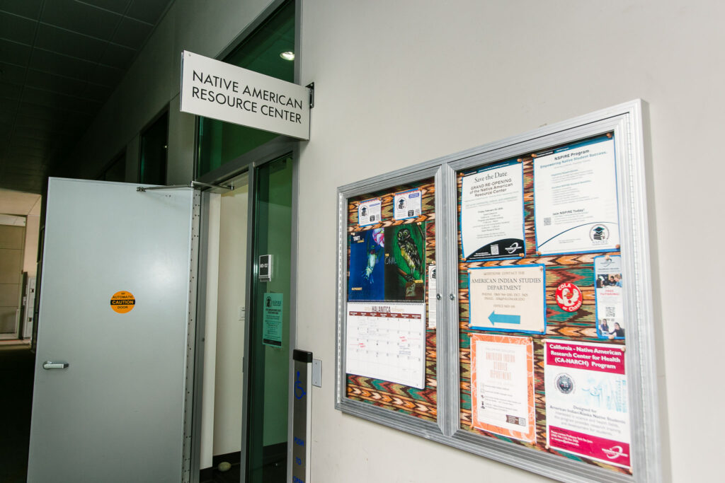 A bulletin board filled with flyers and announcements mounted next to the Native American Resource Center entrance door.