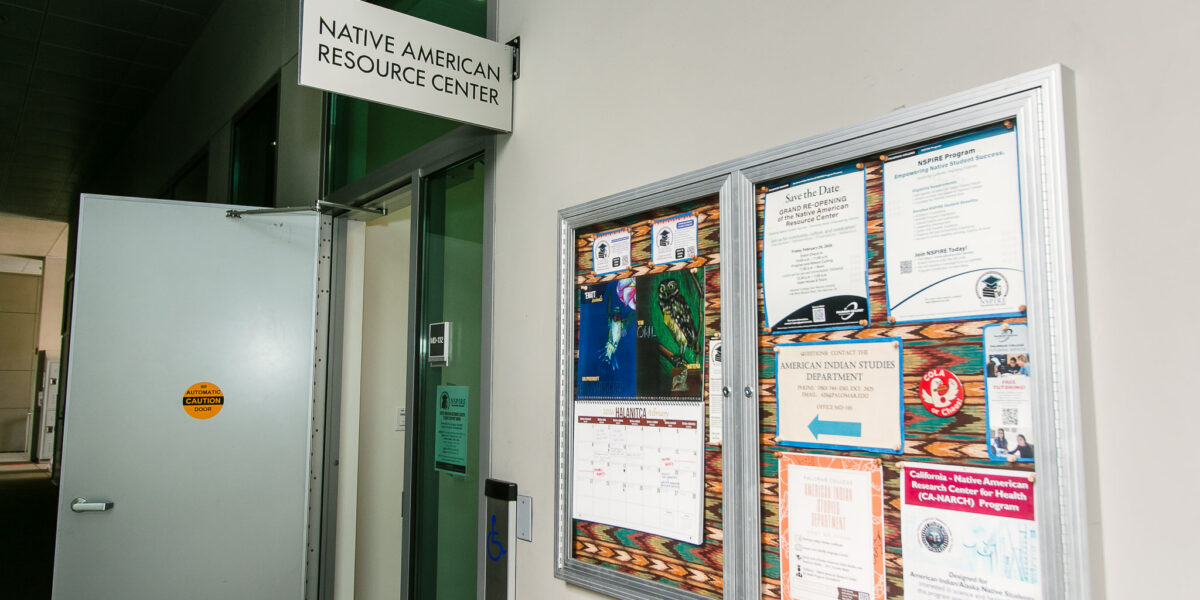 A bulletin board filled with flyers and announcements mounted next to the Native American Resource Center entrance door.
