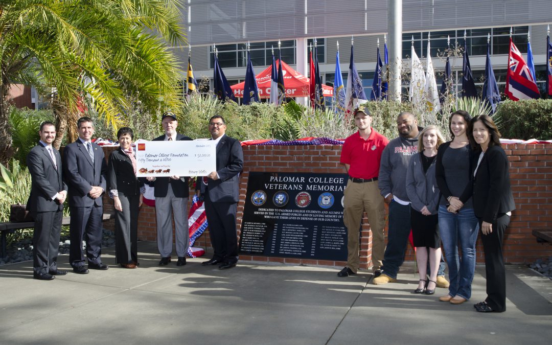 Palomar staff, team and Wells Fargo employees standing in front of the Veterans Memorial holding an oversized check