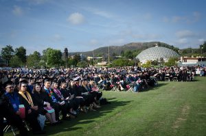 Students in caps and gowns seated at graduation ceremony on the lawn