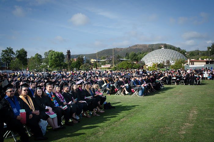 Students in caps and gowns seated at graduation ceremony on the lawn