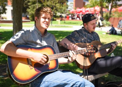 Two students playing guitars on campus
