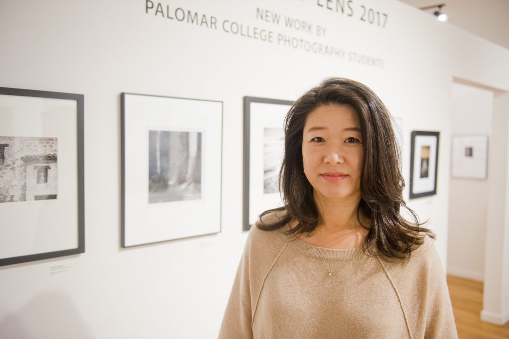Photography instructor Donna Cosentino, standing in a gallery next to framed artwork