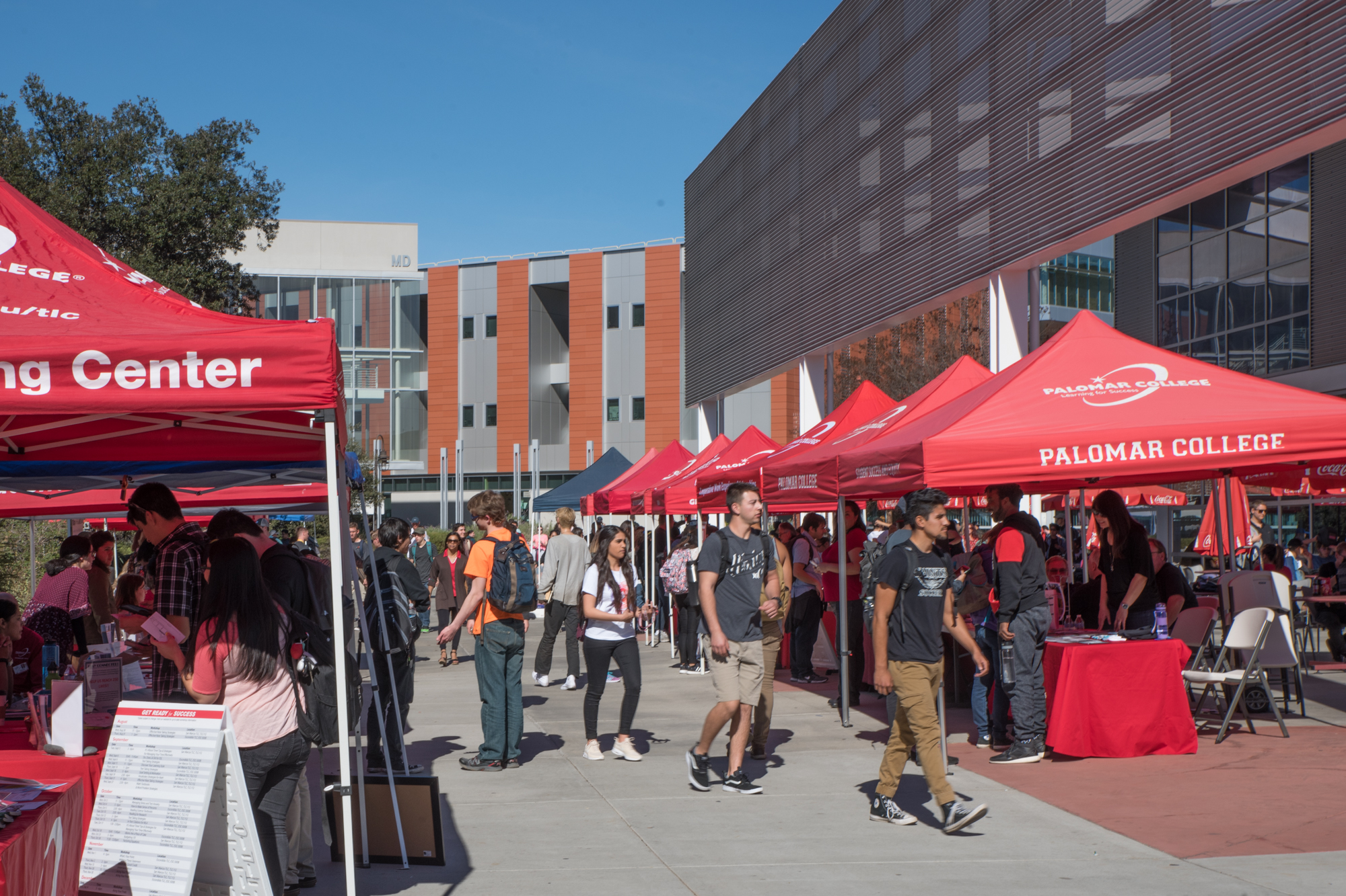 Students walking on campus visiting red Palomar College booths