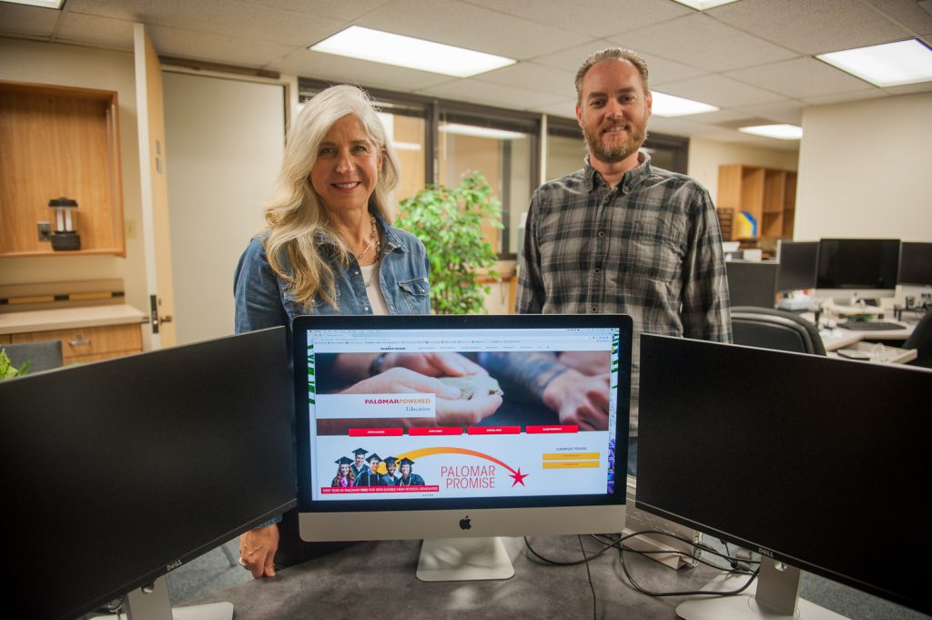 Palomar College webmasters standing behind a computer showcasing a new site design on the screen
