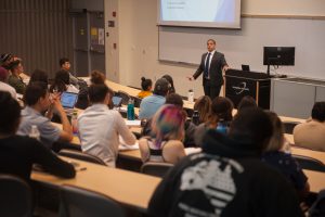 Speaker at the front of an auditorium classroom addressing students