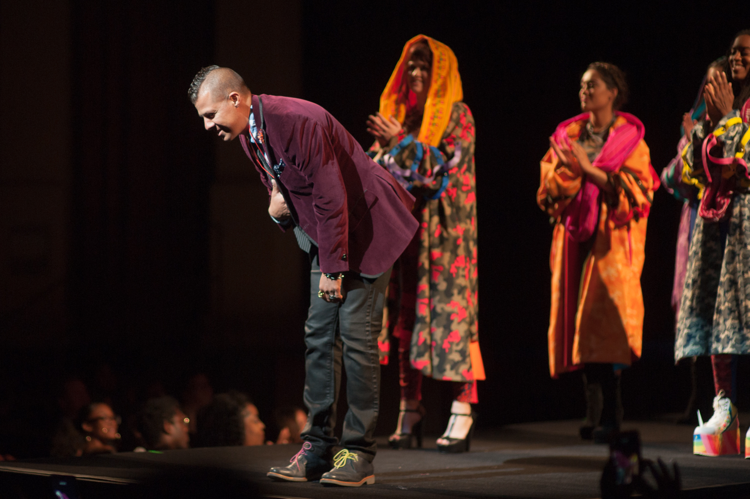 Designer on stage taking a bow with models behind him