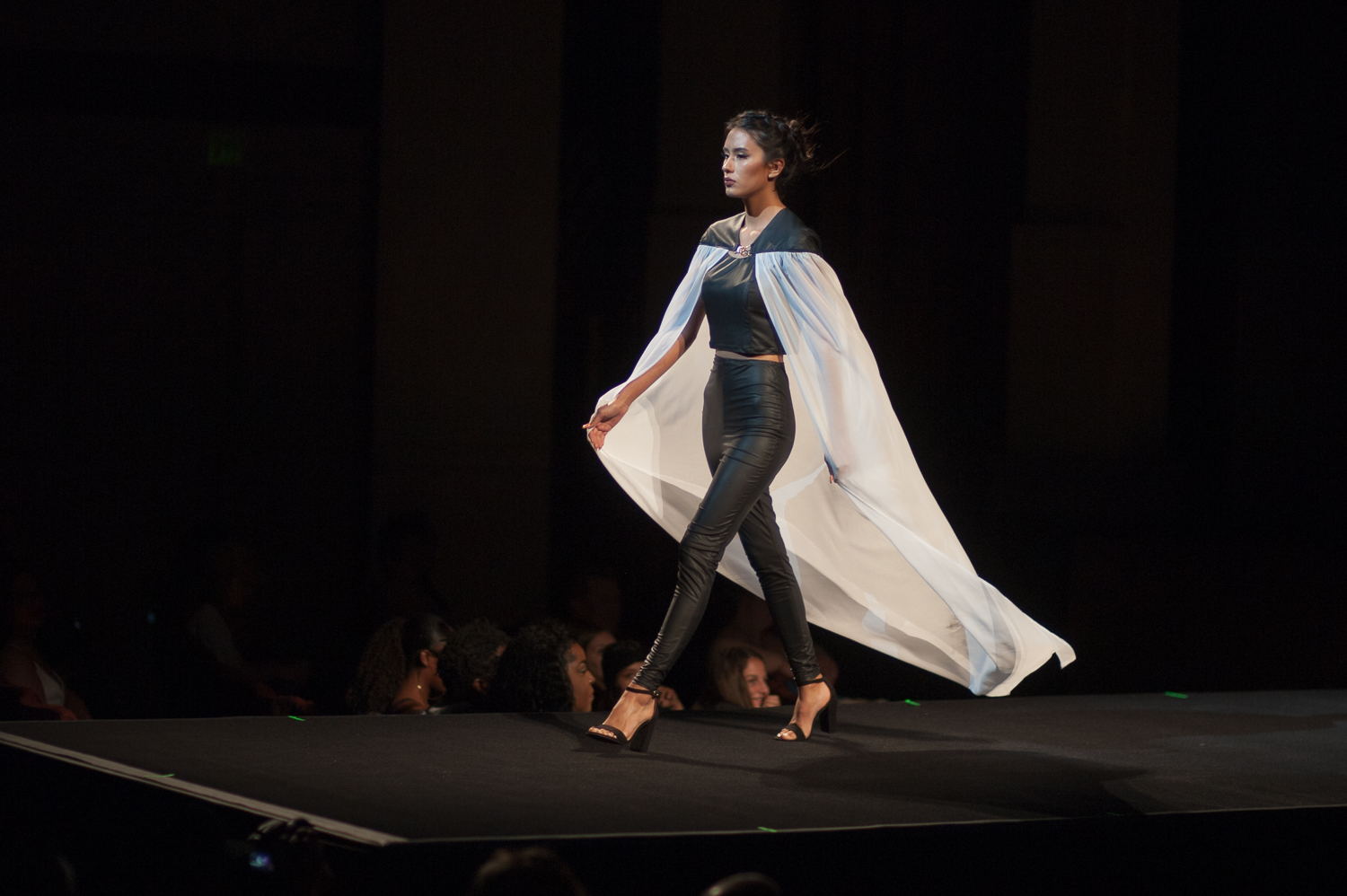Female model walking on runway in a two piece black leather ensemble