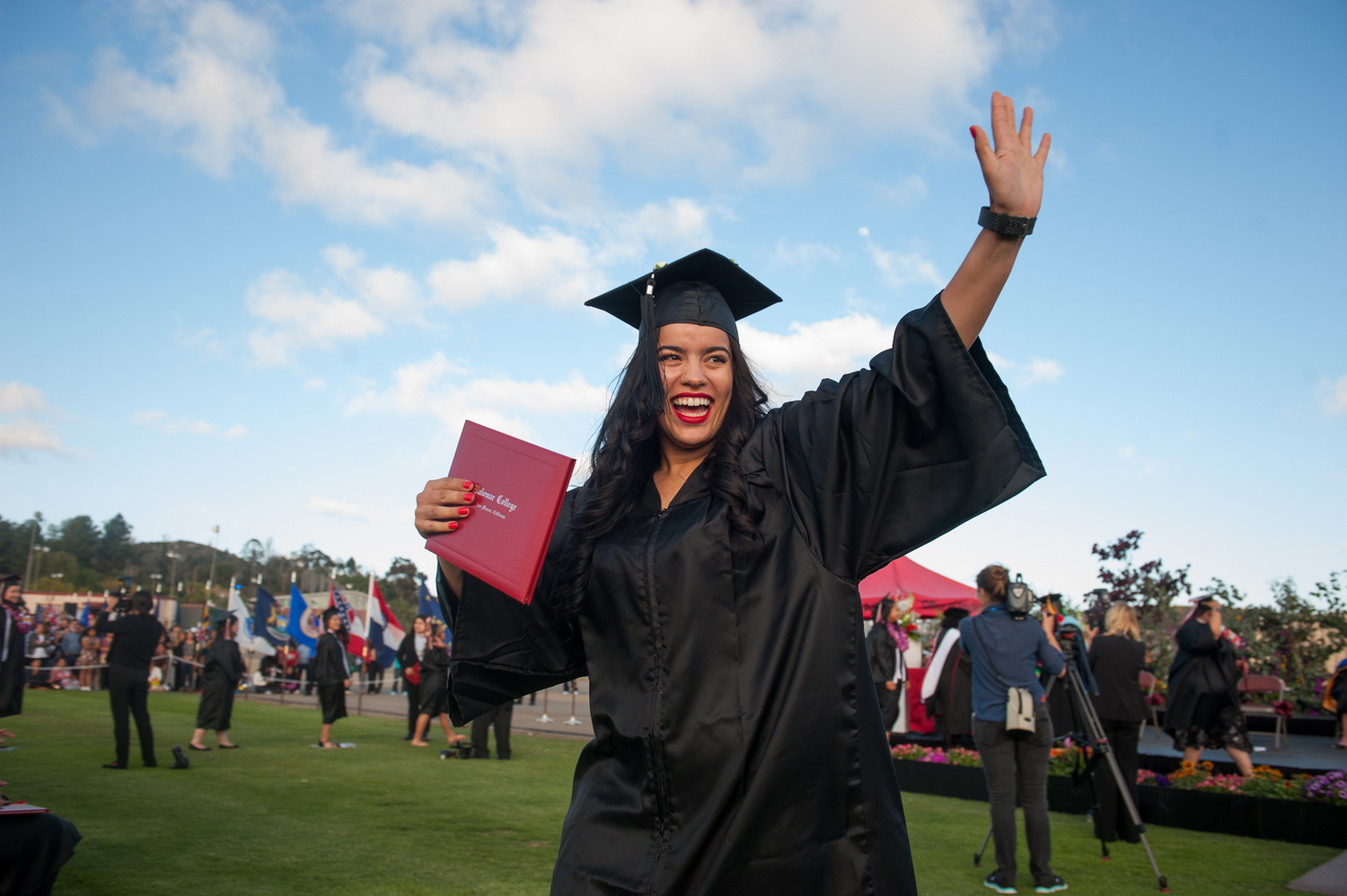 Female graduate holding diploma and waving at commencement