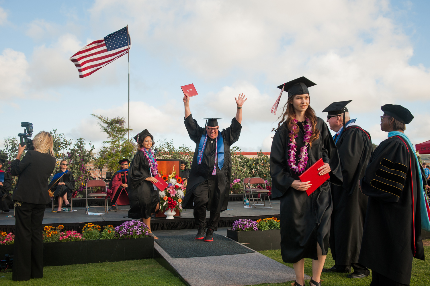 Male graduate celebrating with arms in the air and holding diploma walking off the stage