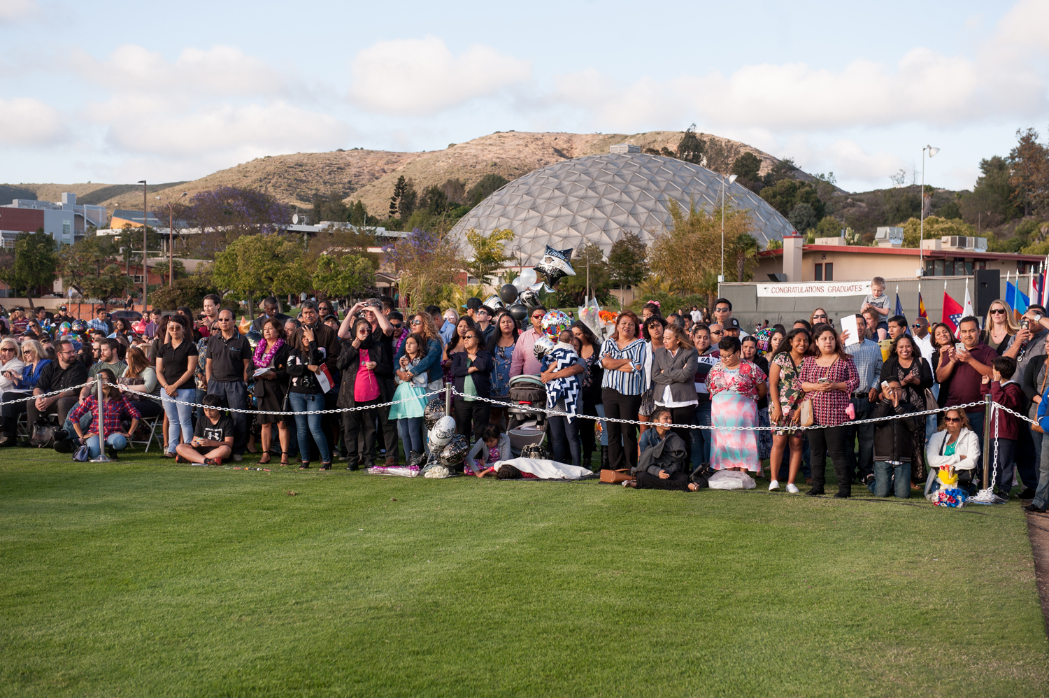 Crowd of friends and family members outside on the lawn attending commencement