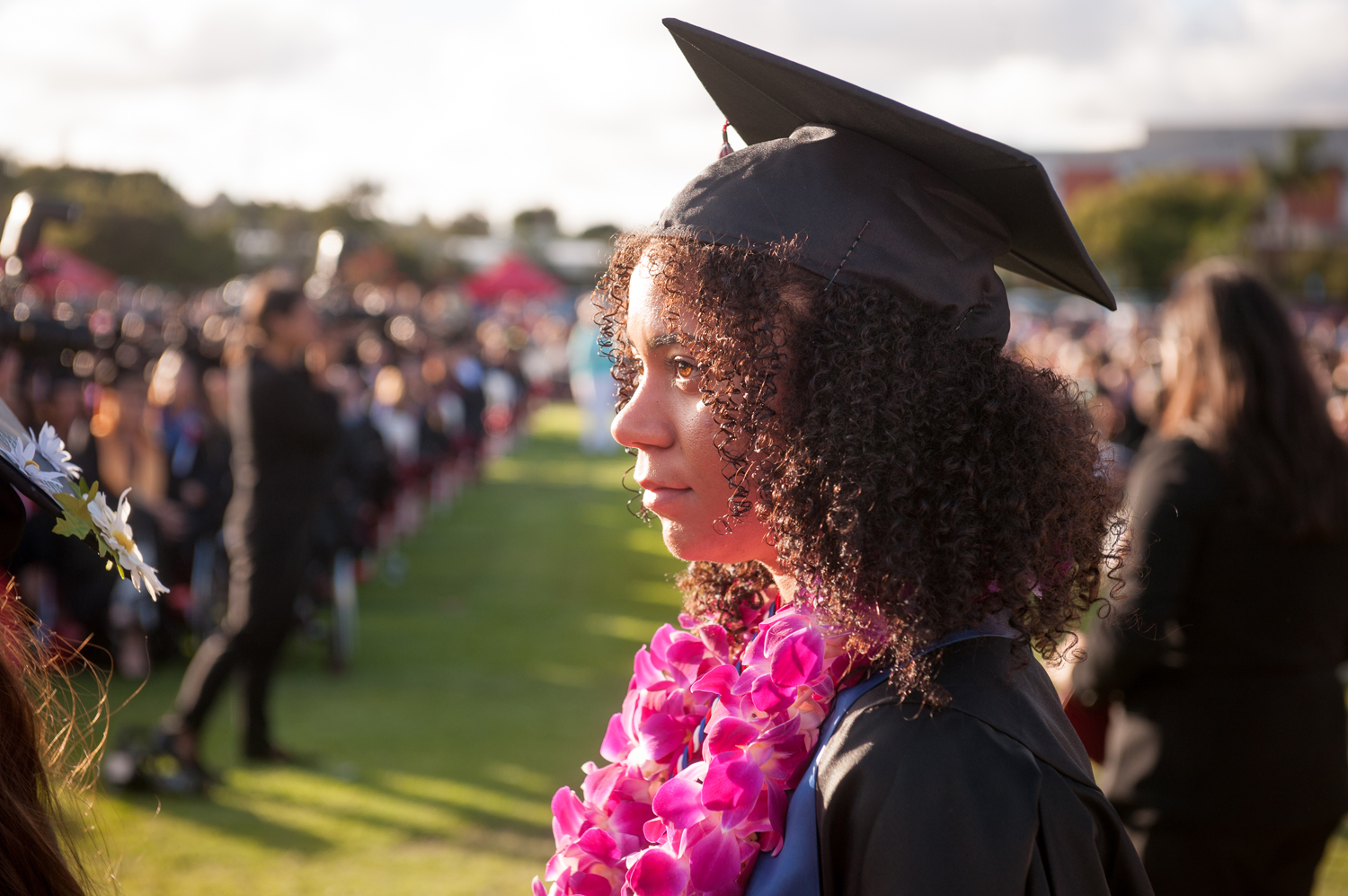Female graduate in gap and gown wearing a floral lei at commencement