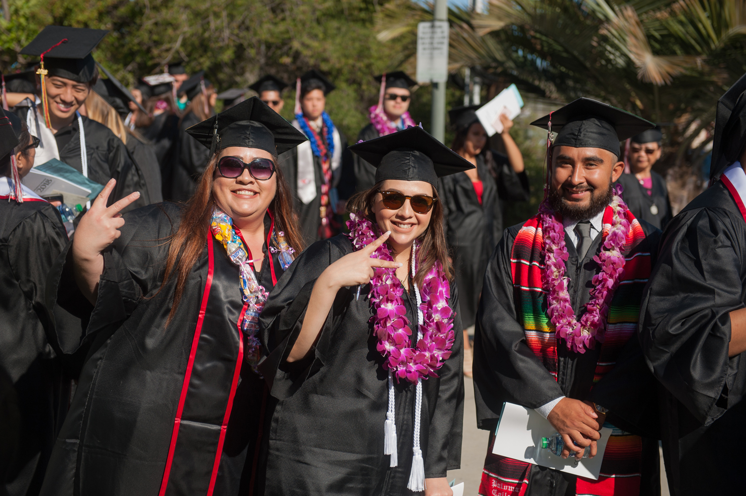 Group of grads, two females doing a peace sign and one male smiling