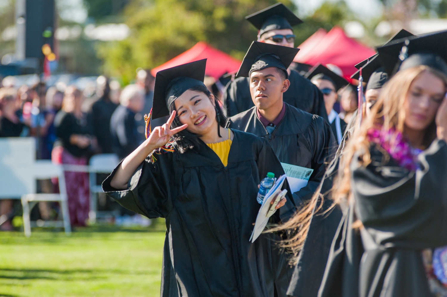 Female grad in cap and gown giving a peace sign at commencement