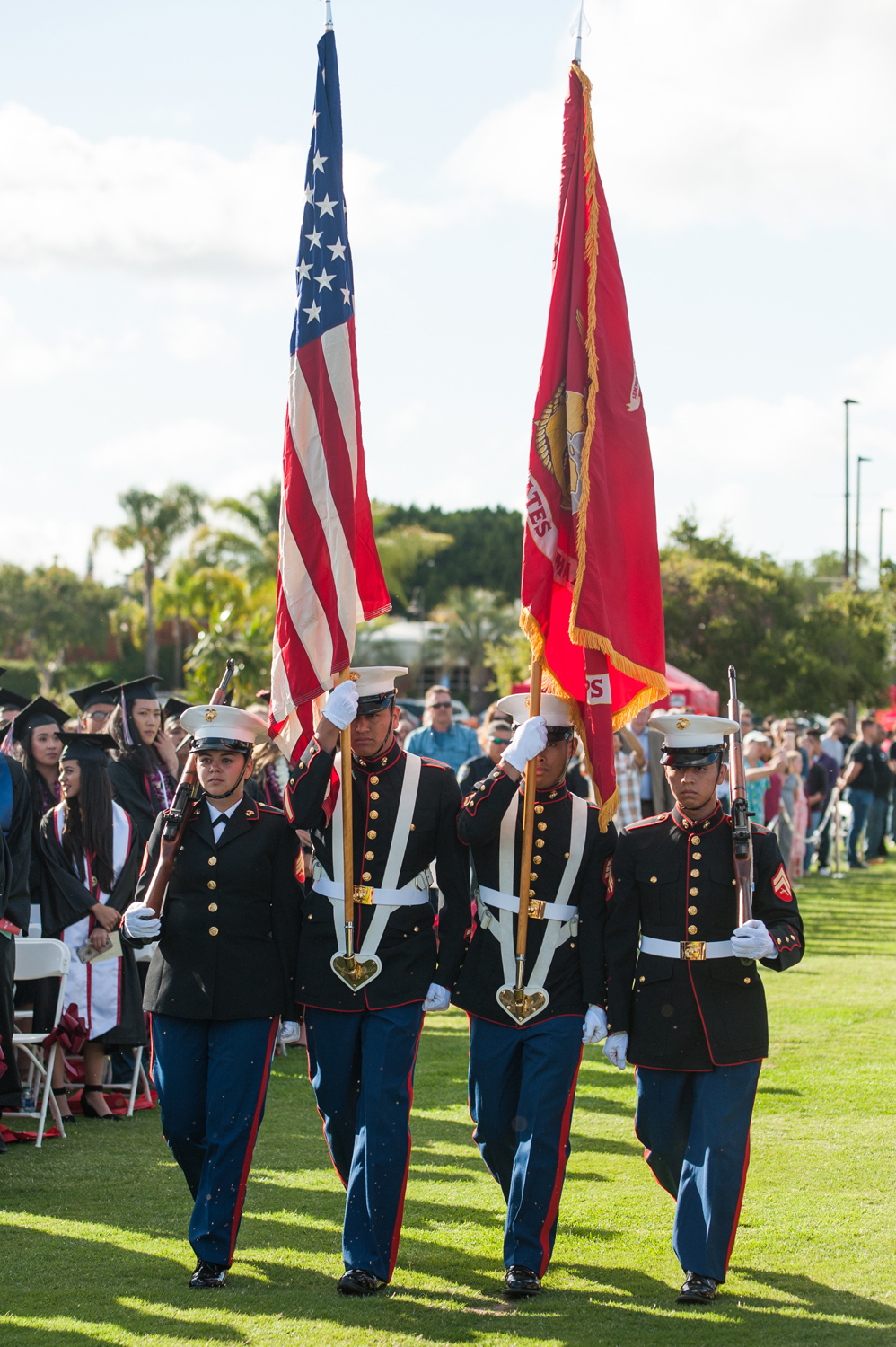 Marines in uniform carrying flags and rifles at commencement