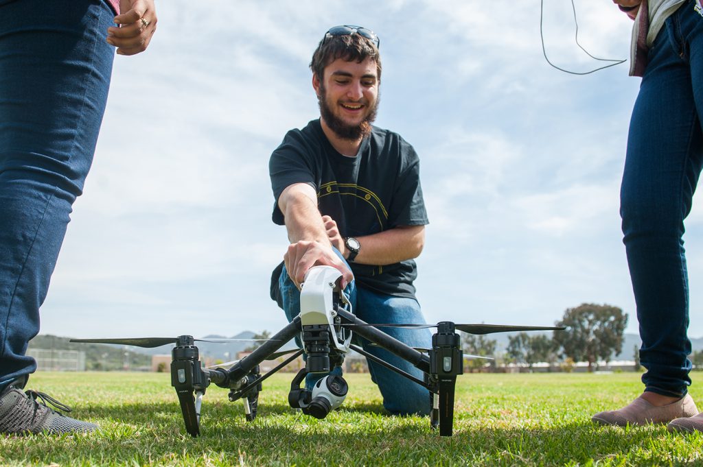 Student holding a drone on a grass lawn in prep to fly