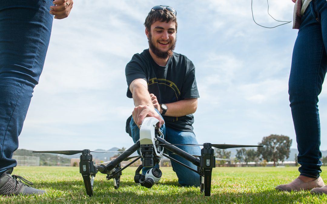 Student holding a drone on a grass lawn in prep to fly