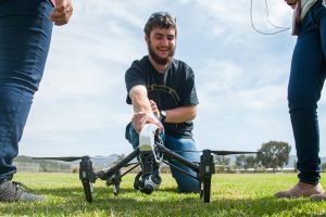 Student holding a drone on a grass lawn in prep to fly