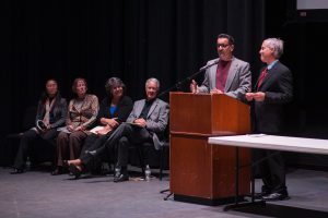 2 speakers at podium with guests sitting near them on stage
