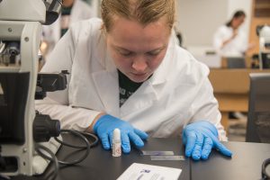 Student in lab coat preparing slides in lab