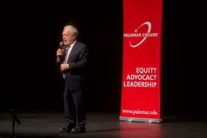 Speaker with microphone on stage in front of a red Equity Advocacy Leadership banner