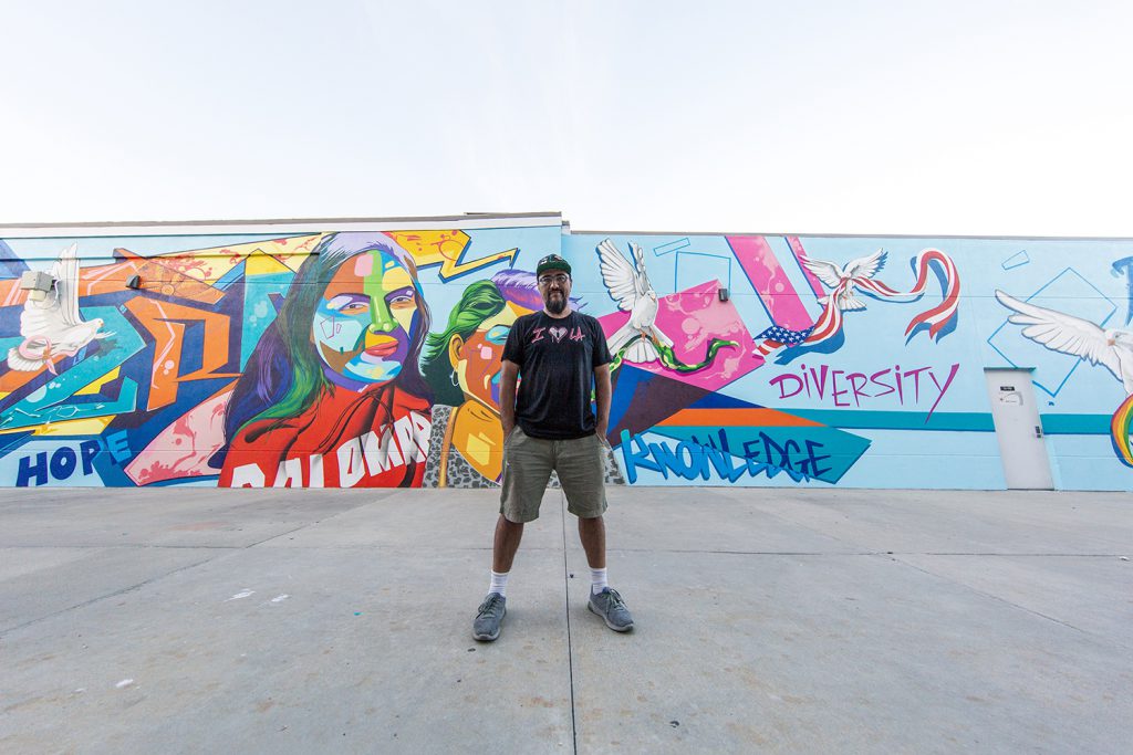 Man One stands in front of the mural he painted at Palomar College