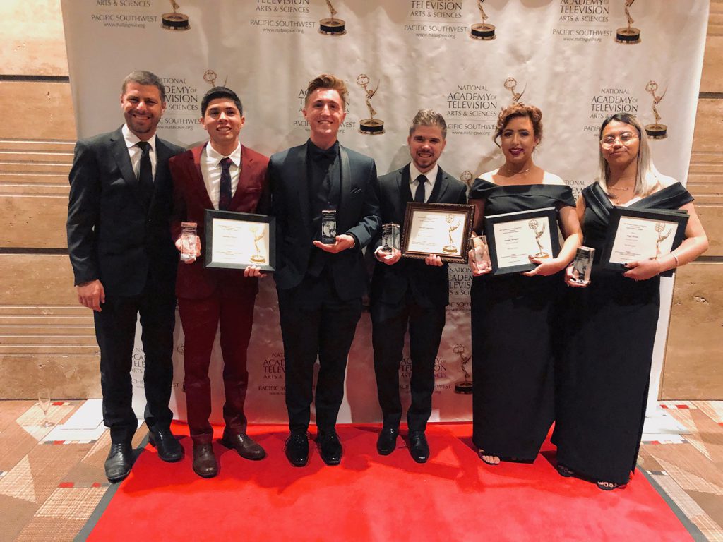 Media studies students and staff in formal attire holding awards on a red carpet