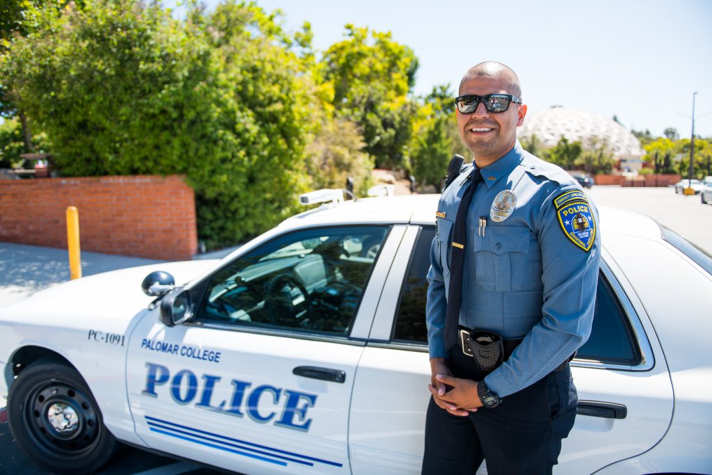Community Service Officer Jesus Montes standing in front of a Palomar College Police car