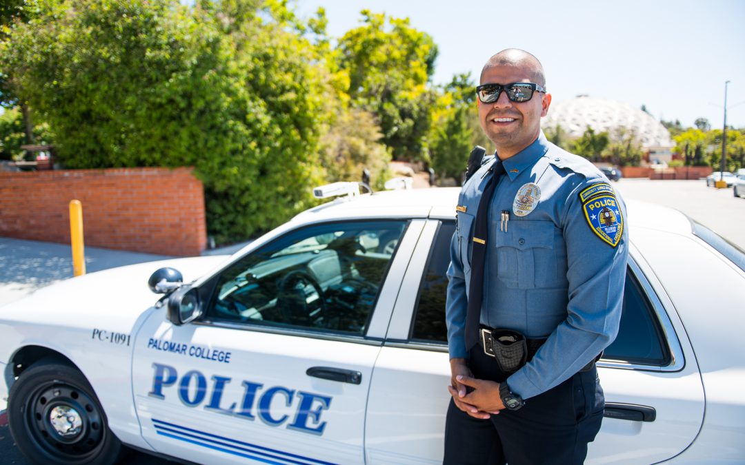 Community Service Officer Jesus Montes standing in front of a Palomar College Police car