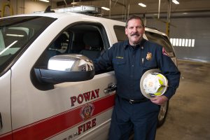 Palomar graduate wearing fire uniform and standing next to a Poway Fire vehicle