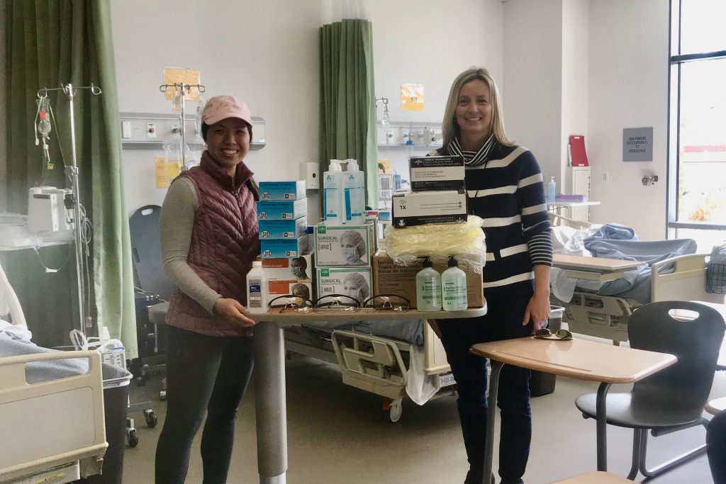 Two adjunct faculty standing next to donated PPC supplies in a hospital room