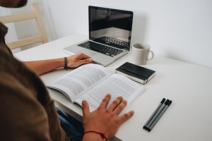 Student sitting at a desk with a book and laptop