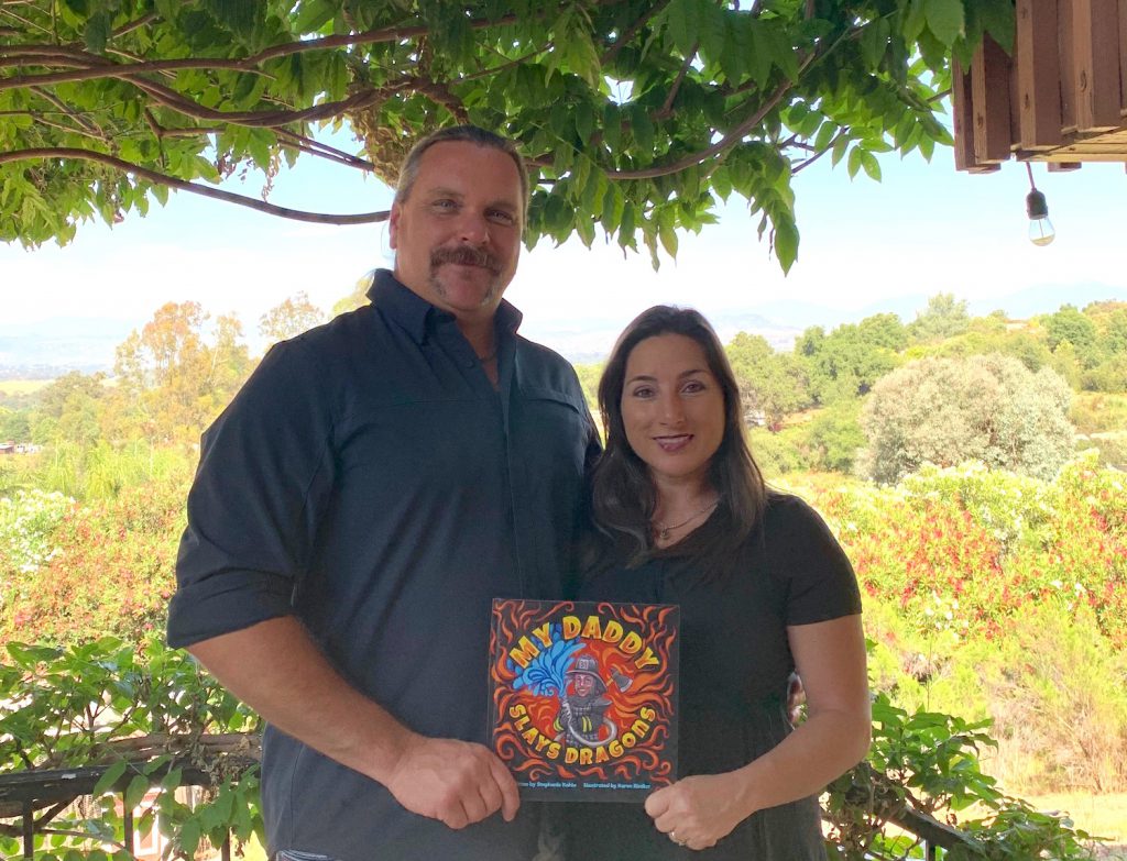 Author and her husband holding the book she wrote called "My Daddy Slays Dragons"