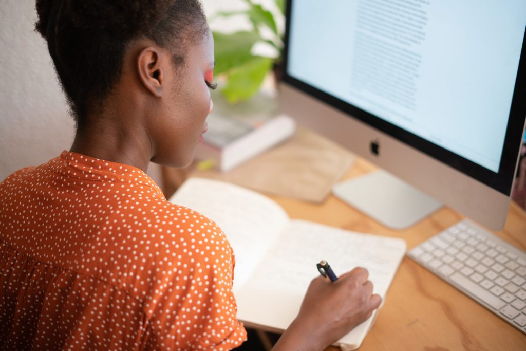 Women writing in notebook in front of a computer