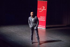 Speaker on stage with a banner for Equity Advocacy Leadership
