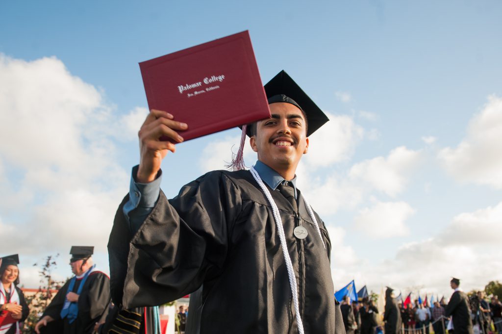 Palomar College student wearing graduation cap and gown and holding a diploma